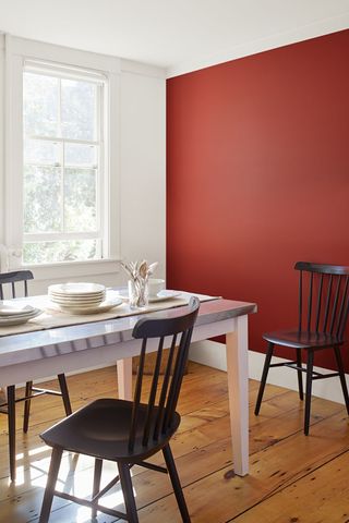 A dining room with a red accent wall and wooden floorboards
