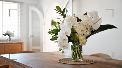 White living room with wooden dining table with a bouquet of white flowers with orchids, roses and lilies to support expert tips on how to make cut flowers last longer 