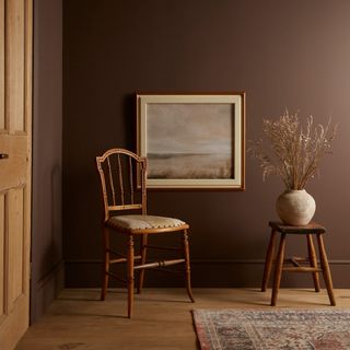 Graham & Brown's paint shade Elderton used on the walls of a room with an antique chair and side table with a vase in front of it and a picture hung on the wall