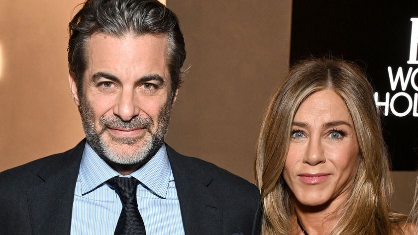 Jennifer Aniston and Jim Curtis dressed up in a dress and suit and tie and staring straight at the camera.