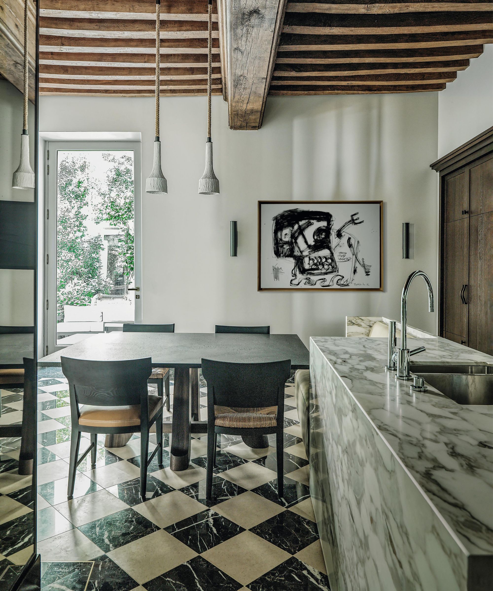 a rustic meets modern kitchen in France with rustic ceiling beams, a marble checkerboard floor and a large marble kitchen island
