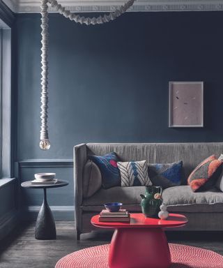 A dark gray living room with a navy sofa and a red coffee table