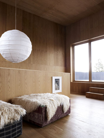 Oak-clad living room, with the individual sitting area covered with sheep skin. On the right wall, there are balcony doors that lead to the outside.