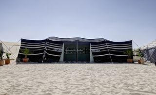 A black Bedouin tent in the desert, at daylight. The tent is set out as a Prada store.