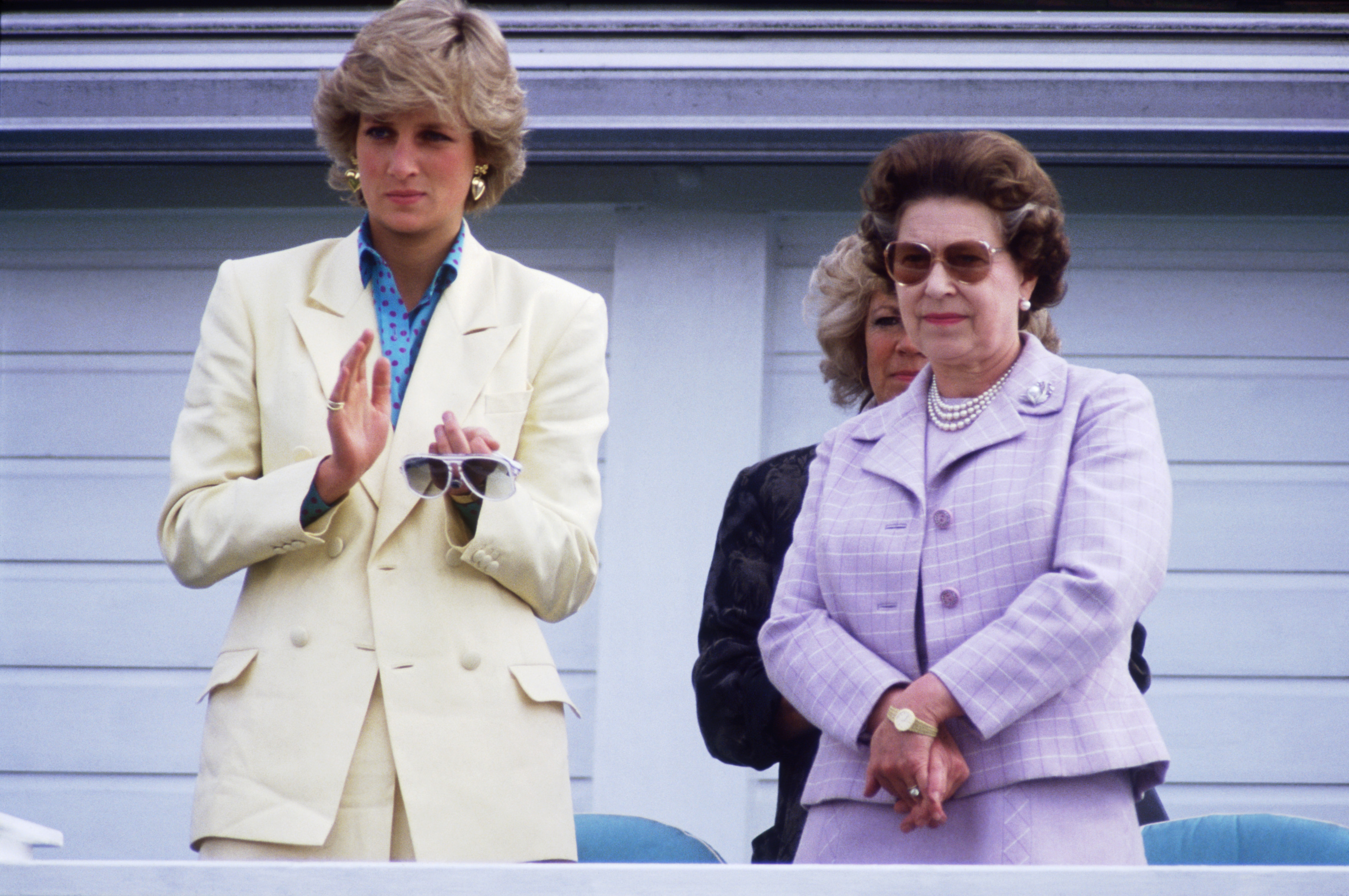 Princess Diana wearing a yellow suit standing next to Queen Elizabeth in a lavender suit