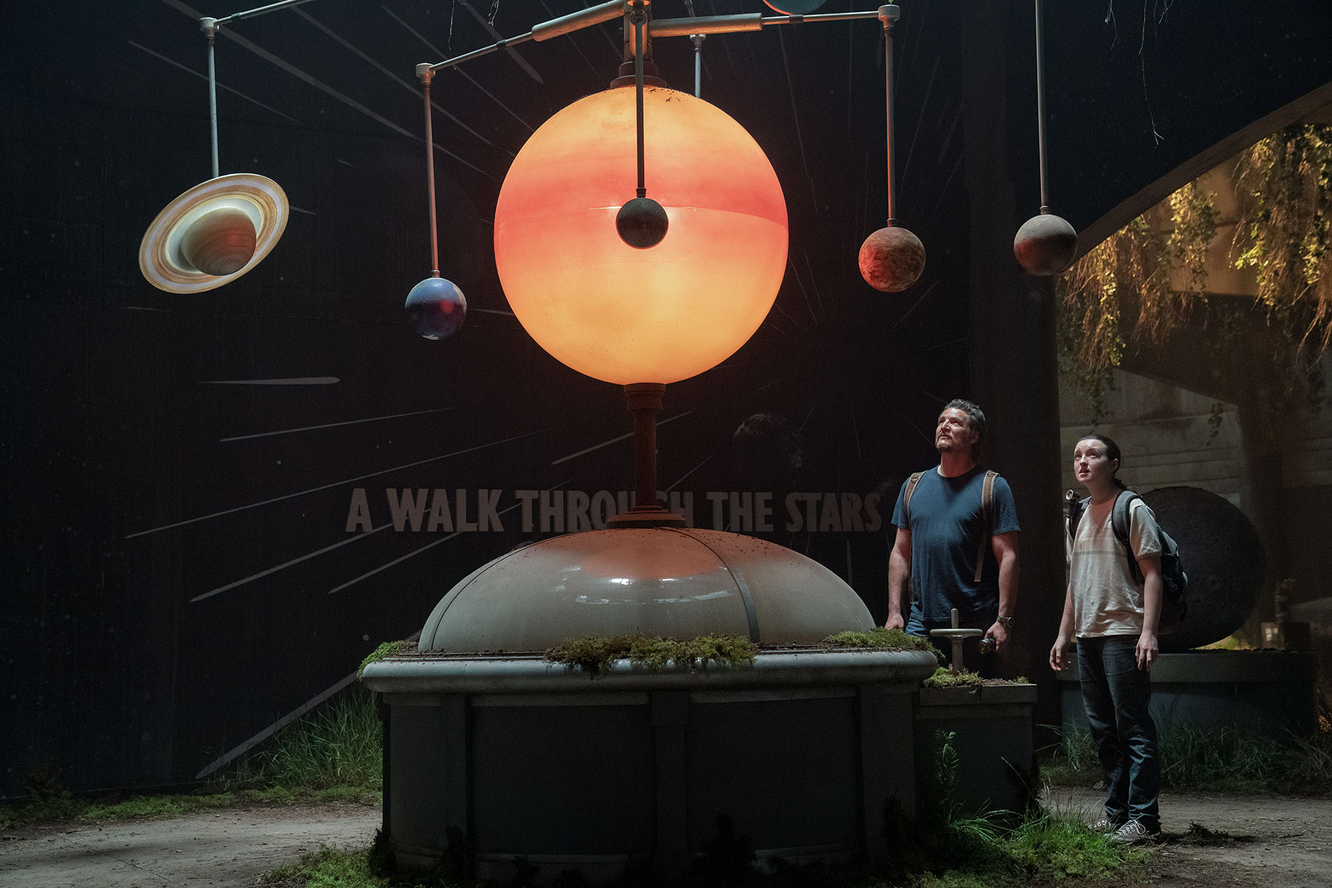 a man and a teenage girl look at a solar system orrery in an abandoned museum