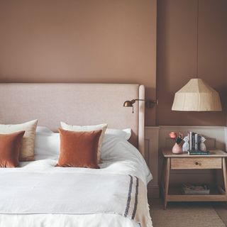 A bedroom painted in light brown with tonal velvet cushions on the bed