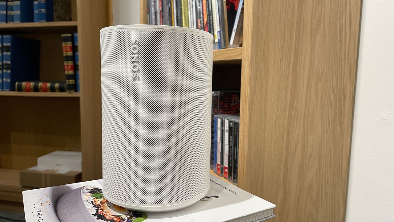 Upright Sonos Era 100 next to a wooden bookshelf