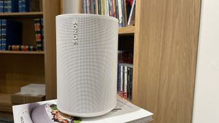 Upright Sonos Era 100 next to a wooden bookshelf