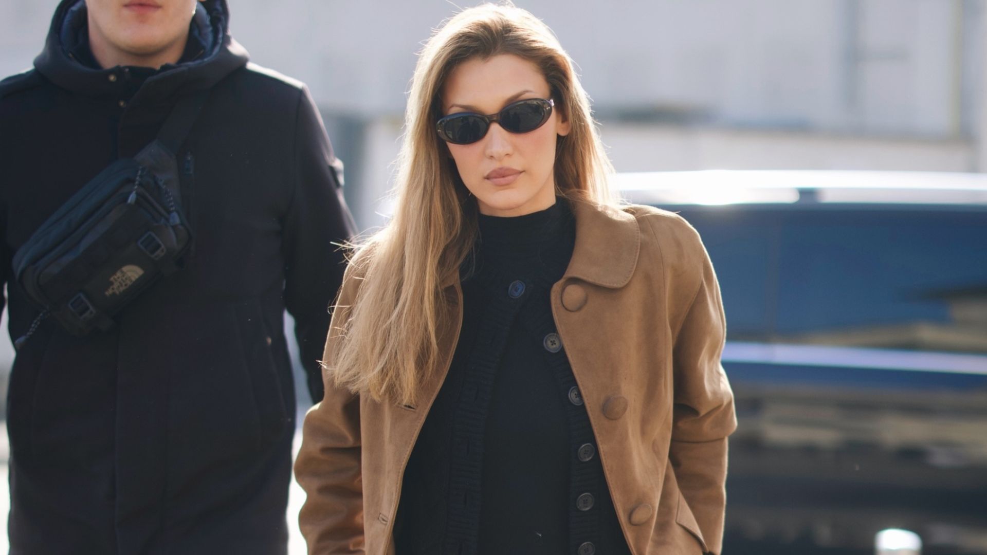 Bella Hadid wears back trousers with black almond-toe boots and suede jacket.