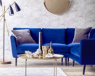 A small corner sofa with blue velvet upholstery in a living room with brass accessories