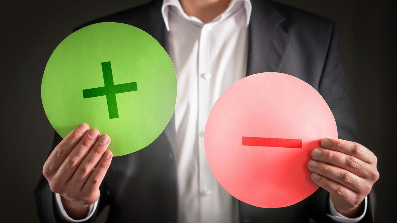 A man holds up a green plus sign and a red minus sign.