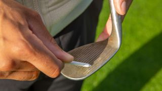 A golfer cleaning the grooves on his wedge