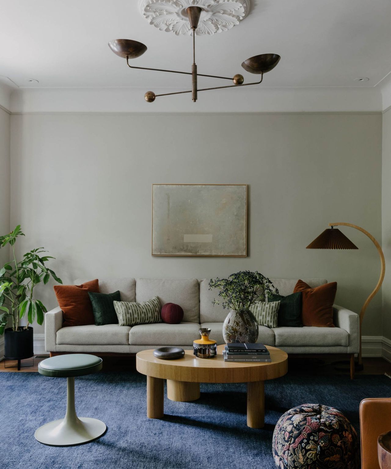A neutral living room with a statement light fixture surrounded by molding, a blue area rug, and a large gray couch