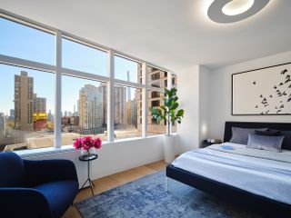 A bedroom with large windows, a blue rug, and a backlit ceiling light