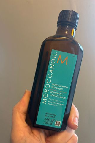 a hand holding a bottle of moroccanoil treatment