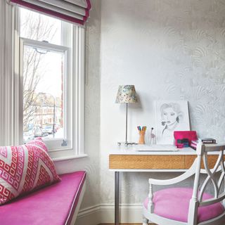 Large bay window with pink seat cushion, next to a desk with a matching pink cushioned chair and accessories on the desk