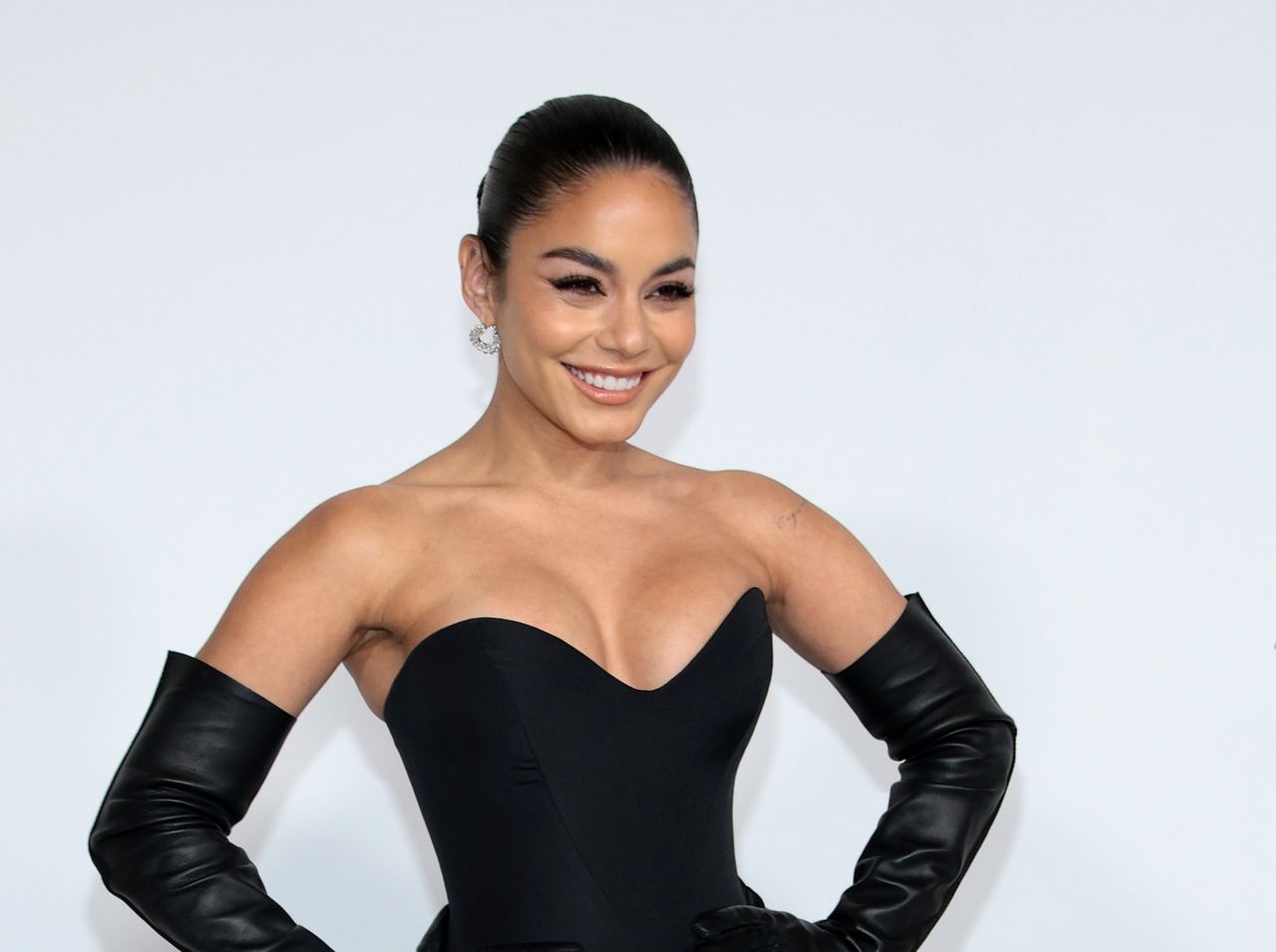 A headshot of Vanessa Hudgens smiling in a black strapless dress 