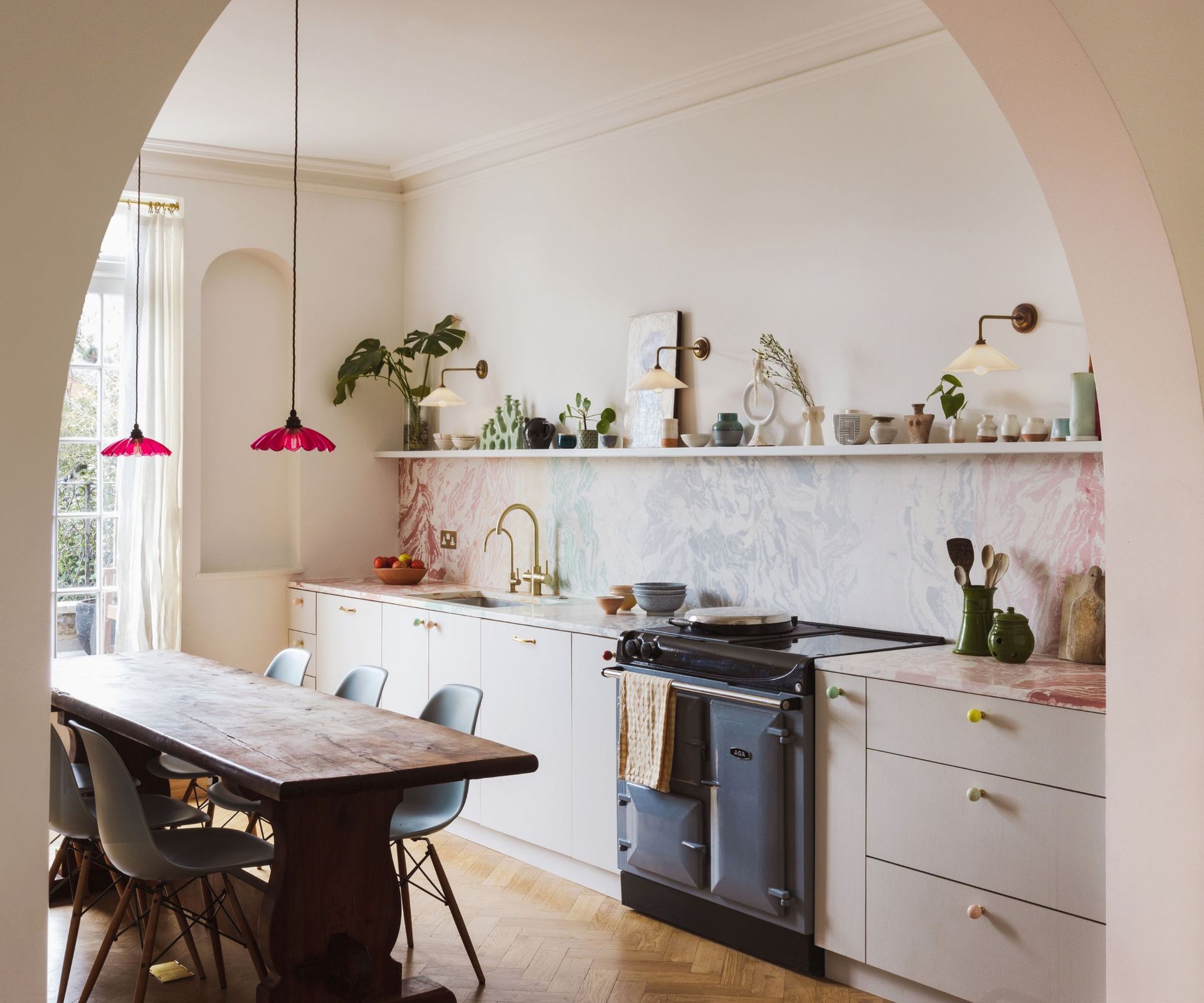 A galley kitchen with white cabinets, colorful marble countertops, and a kitchen table at the center