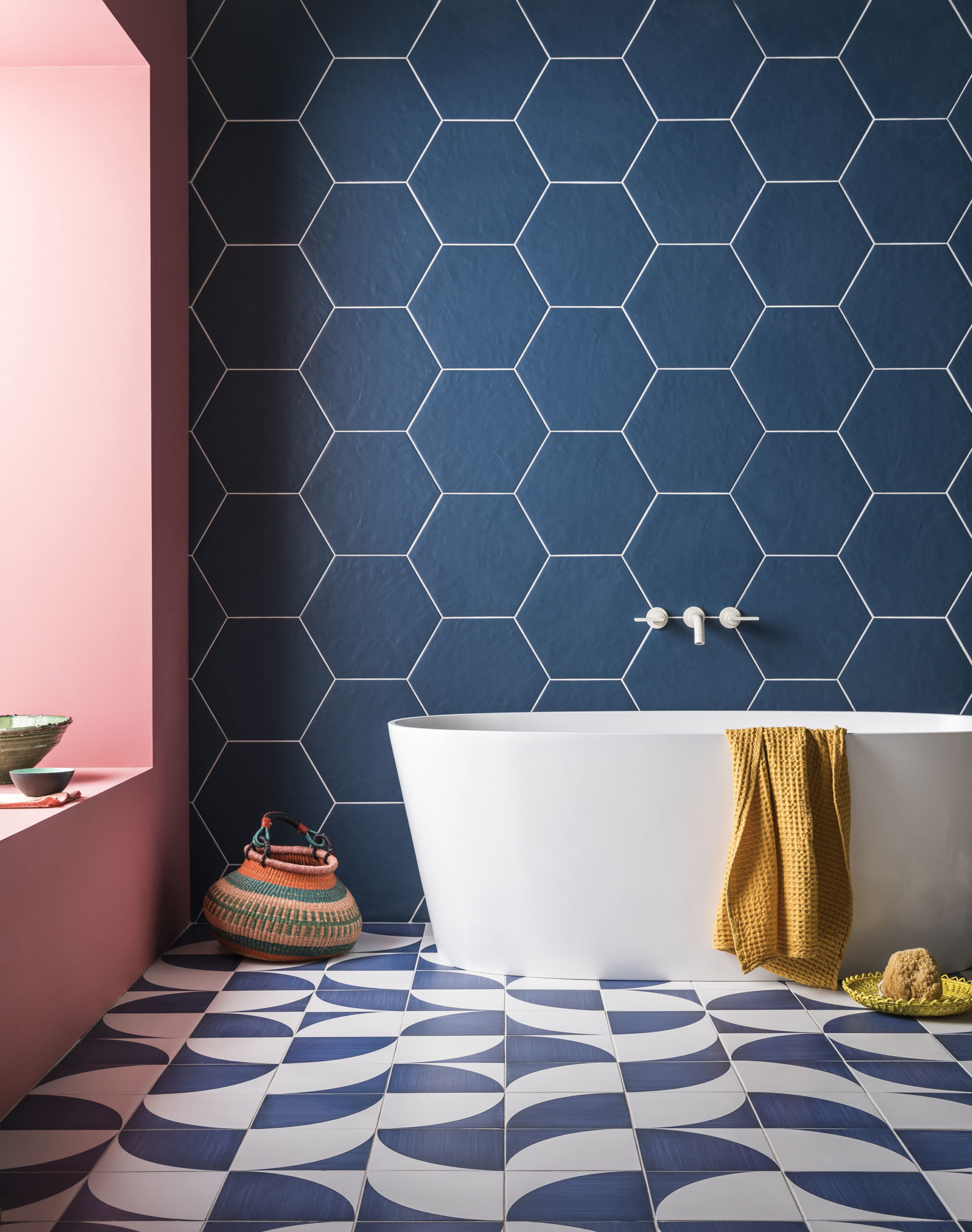 Blue hexagonal wall tiles behind a white bath and blue and white floor tiles.