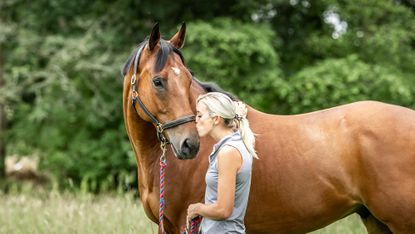 Woman kissing horse on the nose in a field in summer