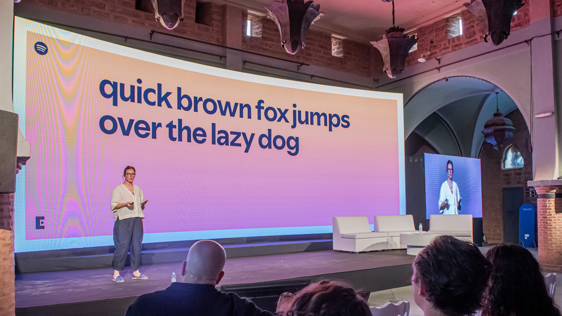 &#039;quick brown fox jumps over the lazy dog&#039; on the screen with a woman talking on a stage 