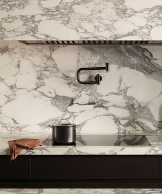 A marble countertop and backsplash with a built-in stove and pot filler