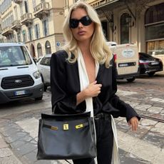elsa wears oversize sunglasses, a black top, black jeans, and a white silk scarf.