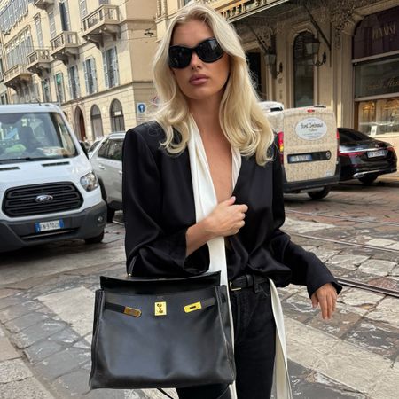 elsa wears oversize sunglasses, a black top, black jeans, and a white silk scarf.