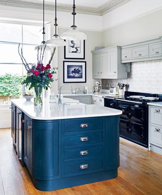 An example of kitchen cabinet ideas showing a curved island with blue cabinets and a white worktop