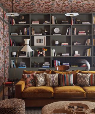 A boldly patterrend living space with built-in dark wood book shelves and a mustard sofa