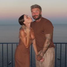 Victoria Beckham poses for a photo with David Beckham wearing a dark brown slip dress.