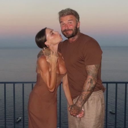 Victoria Beckham poses for a photo with David Beckham wearing a dark brown slip dress.