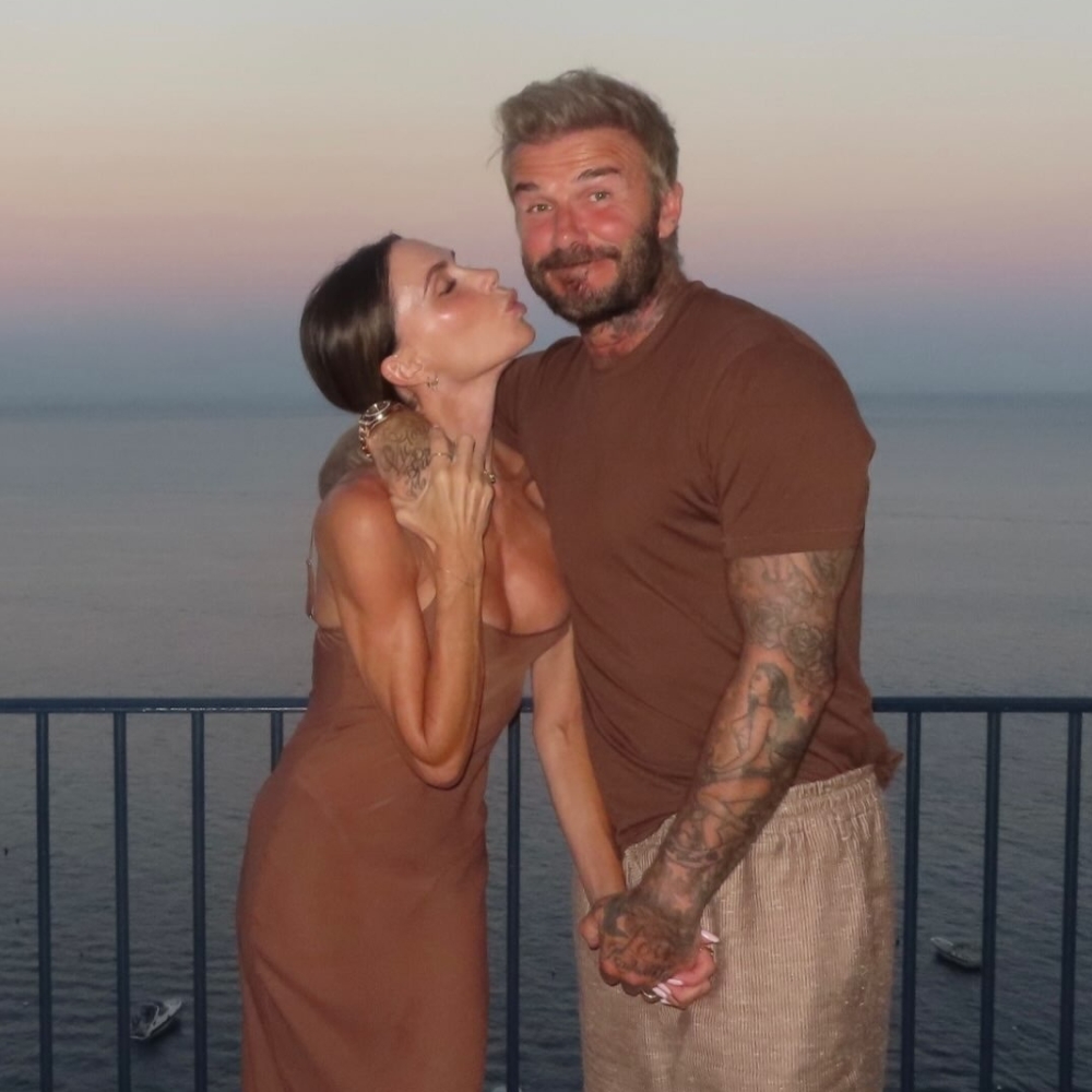 Victoria Beckham poses for a photo with David Beckham wearing a dark brown slip dress.