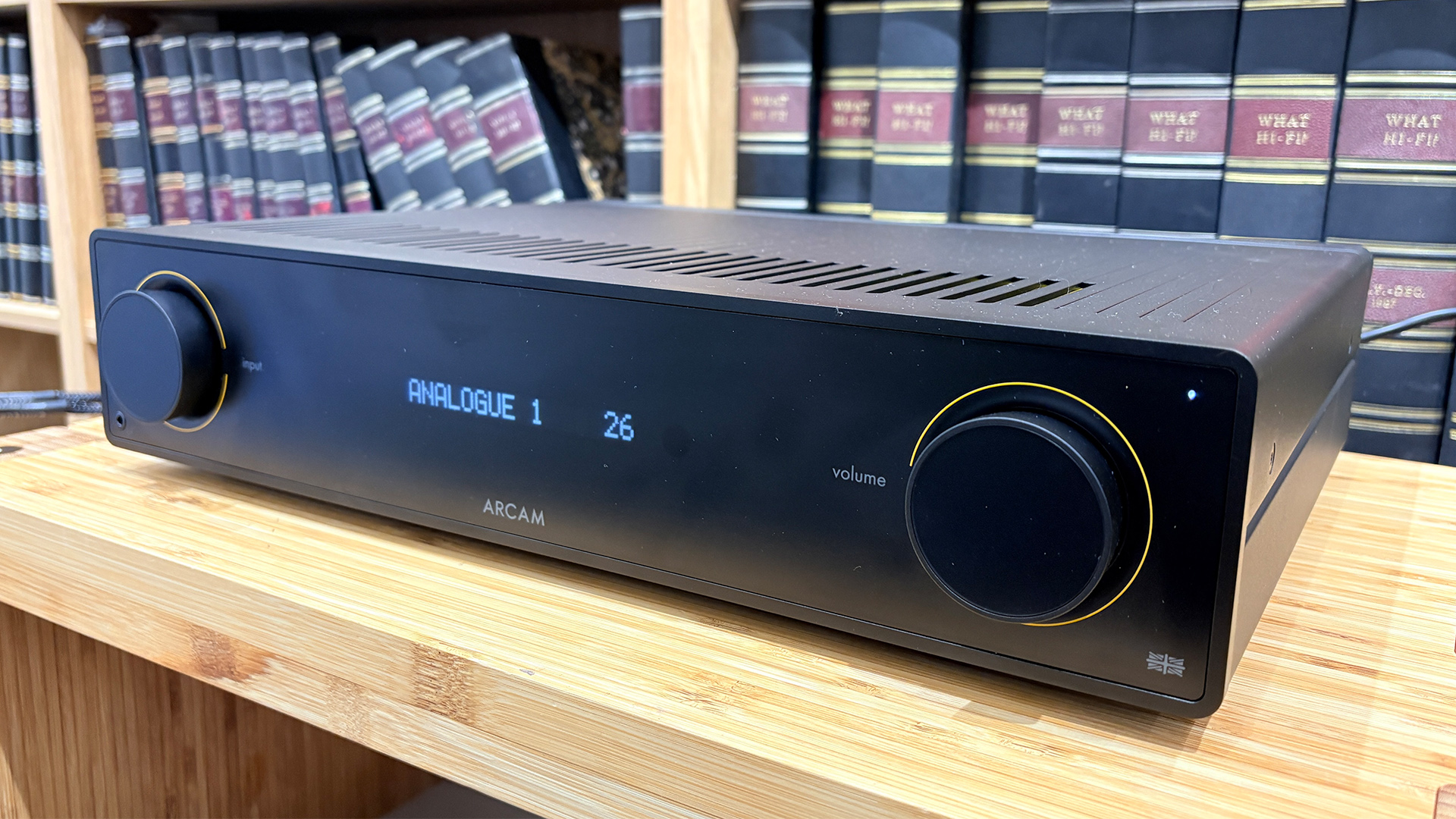 Arcam A15+ integrated amplifier on wooden AV rack in front of bookcase