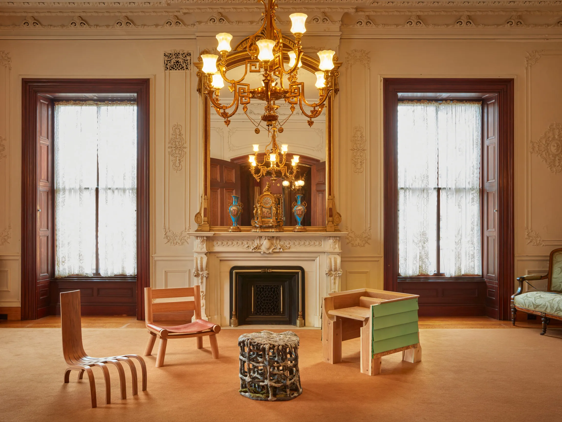 A quirkily decorated, palatial living room is filled with a contrasting mixture of whimsical home additions and classical chandeliers, stuccoed detailing, and velvety armchairs.
