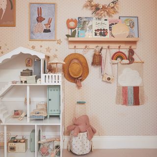 A children's playroom with a dotted wallpaper, a dolls house and a shelf with hooks displaying books, toys, decor and a hat