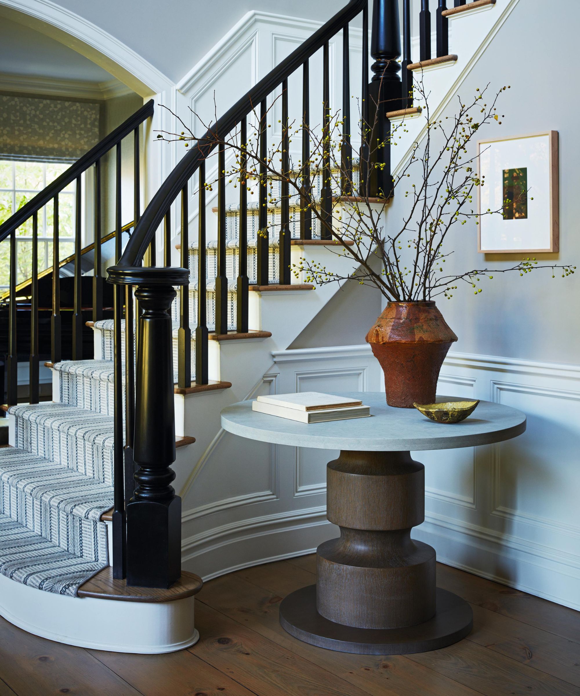 a large traditional colonial staircase with dark painted curved banister, dark wooden floors, a round hall table and a striped runner