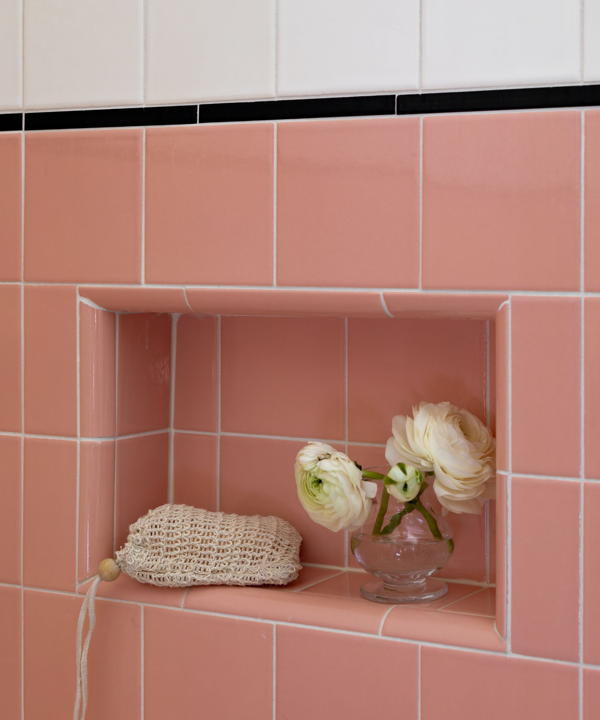 pink tiled shower with a storage niche with a small bud vase and a soap in a mesh bag