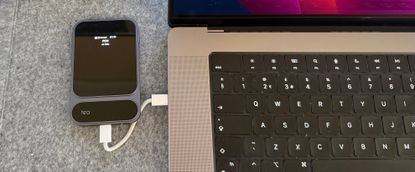 Photograph of the Khadas Tea Pro Headphone Amplifier on a grey fabric surface next to a MacBook Pro