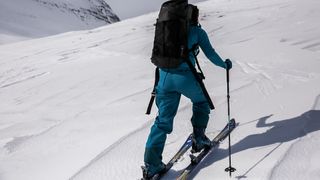 A woman on a snowy ski slops, skiing away from the camera, wearing a pair of Patagonia Women’s Storm Shift Pants.