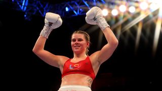 Boxer Savannah Marshall raises her white gloves celebrates above her head in victory, following her previous Super-Middleweight win.