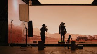 Astronaut on the set of movie set on Mars, with a cameraman shown filming the scene.