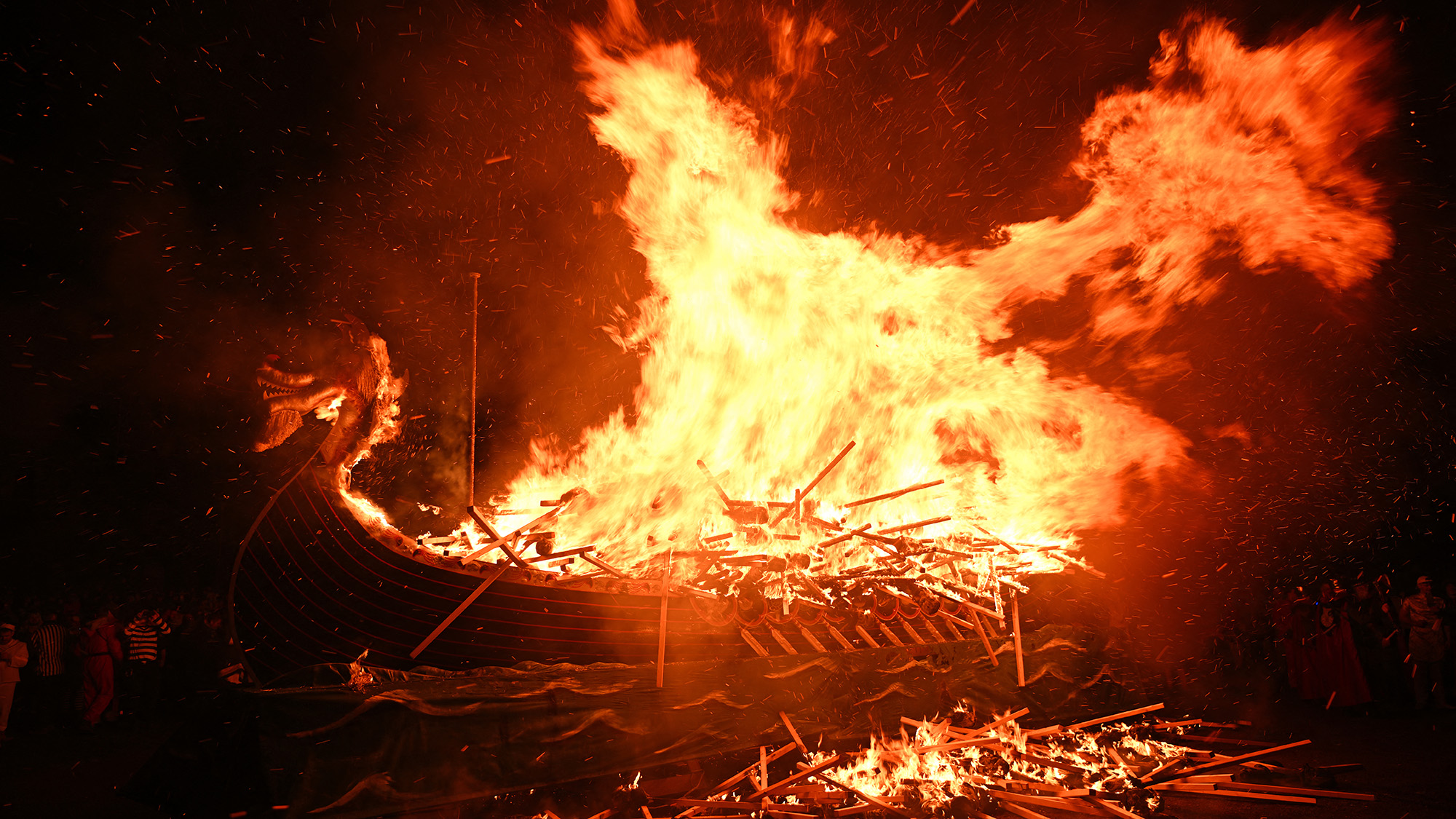A large wooden Viking boat floats while being on fire.
