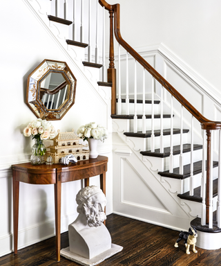 A white and wood staircase in an entryway with an antique table and mirror.