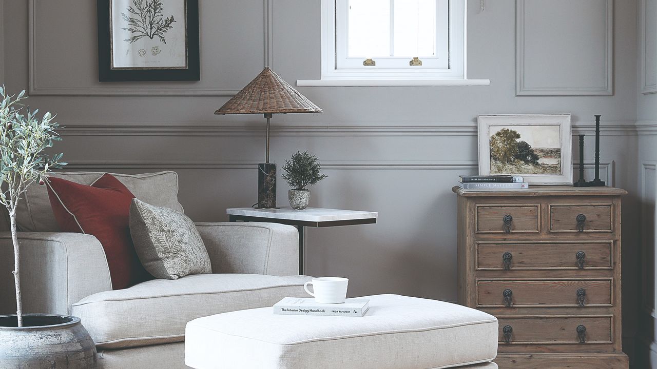 A grey-painted living room with wall panelling and cream armchair with a matching footstool