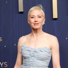 a woman with short, blonde hair wearing a baby blue gown taking a photo in front of a blue background