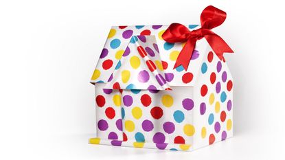 A wrapped gift with a red bow is shaped like a house.