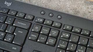 a black full sized keyboard with batteries and a palm rest on a clean beige surface with a blue backdrop