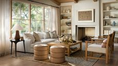 neutral farmhouse living room styled around a large fireplace with a sofa, two ottomans, a wooden coffee table and armchairs on a rug